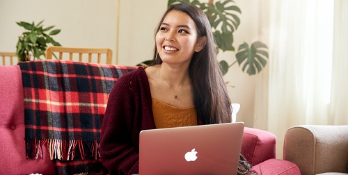 Student sitting on a comfy sofa with her laptop open on her lap. 